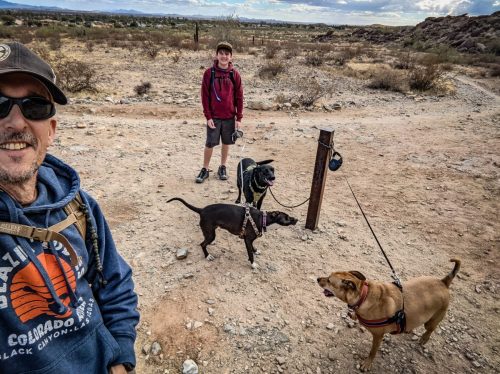 A selfie on a desert trail with a hiker, a black dog and Ari